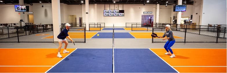 Two players rallying across an indoor Crush Yard pickleball court