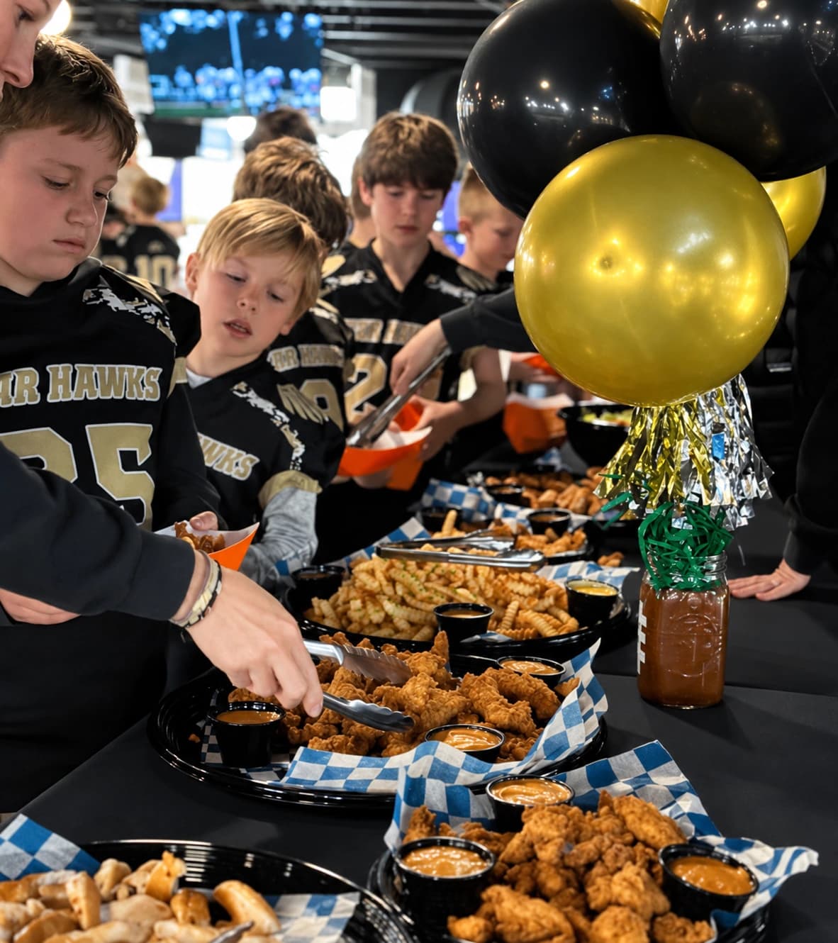 Kids enjoying a birthday buffet beside black and gold balloons