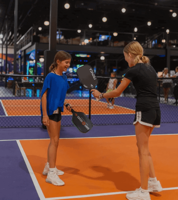 Two young people playing pickleball on an indoor court, both holding paddles and smiling.