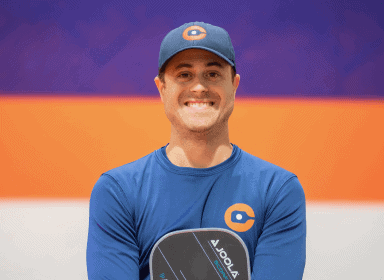 Man in a blue shirt and cap holding a paddle, standing against a colorful background, smiling.