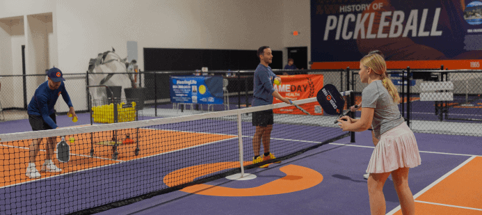 Three people playing pickleball indoors on a marked court.