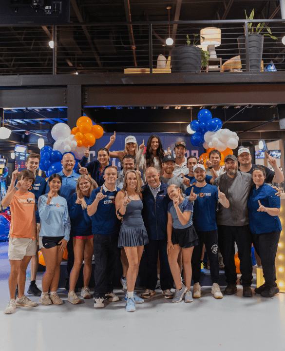 A group of people posing together indoors, surrounded by blue and orange balloons.